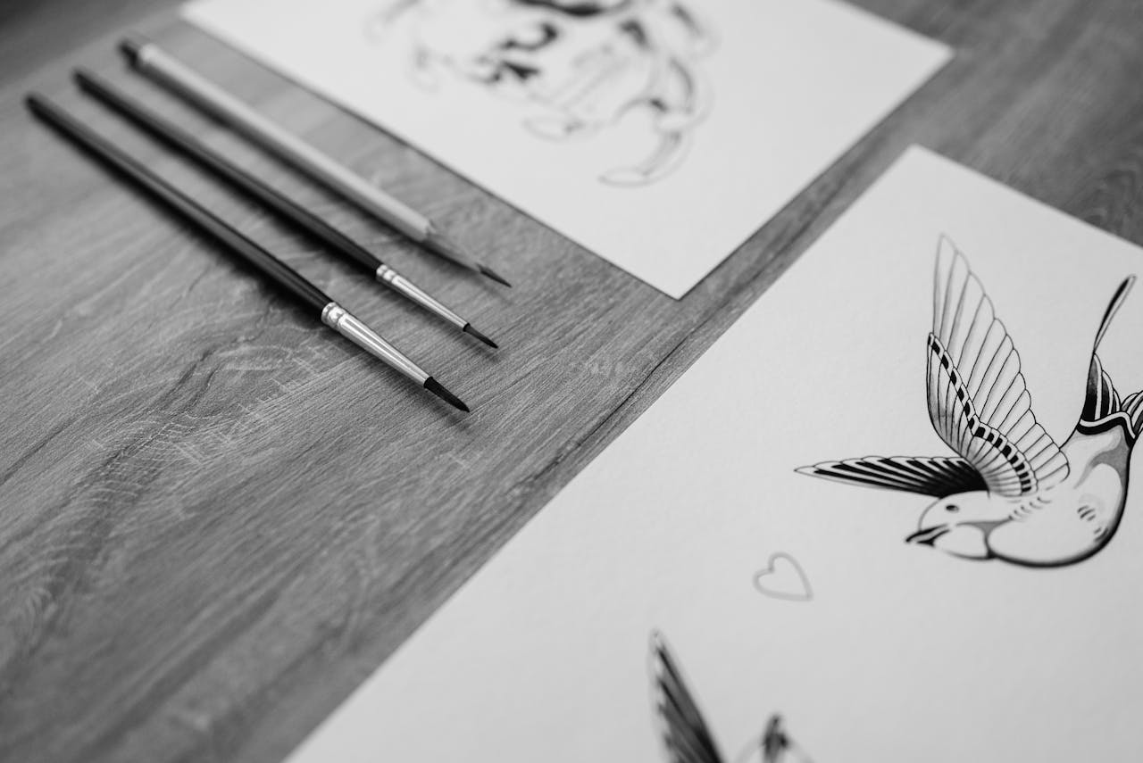 Black and white art sketches with brushes on a wooden table.